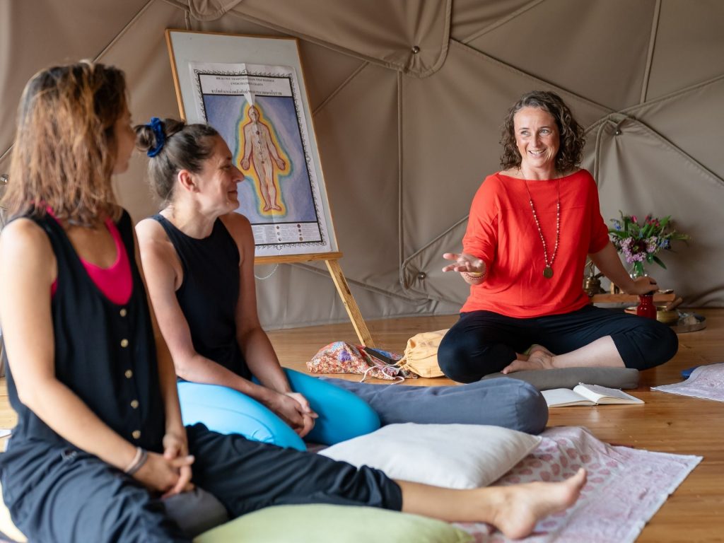 Katrin talking to two of her students in Thai Massage class, with a chart of the Sen lines in the background