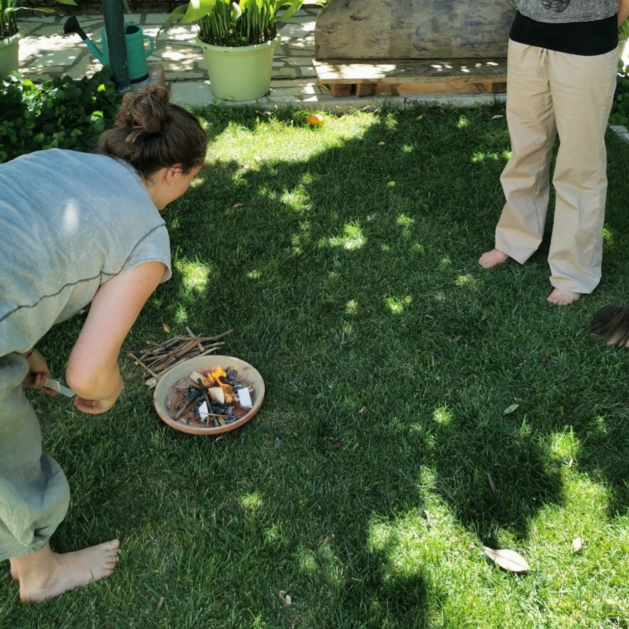 Katrin putting small folded pieces of paper into a small bowl with a fire